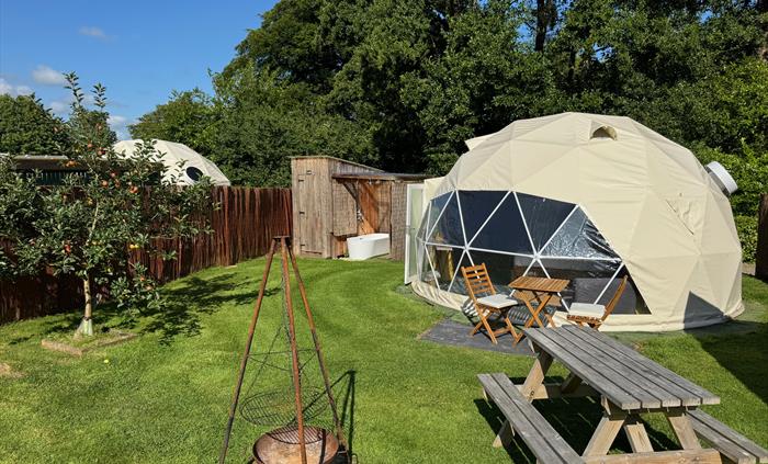 A 5m dome, fully insulated, set in its own garden with picnic table, Firepit and outdoor furniture. An open air deep bathtub can be seen in the backgr